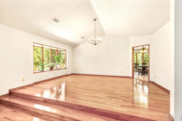 spare room featuring a notable chandelier, a textured ceiling, vaulted ceiling, and hardwood / wood-style flooring