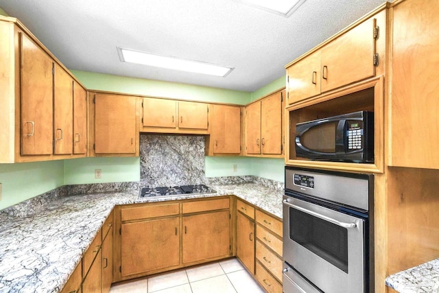 kitchen with light stone counters, light tile patterned floors, a textured ceiling, stainless steel oven, and gas cooktop