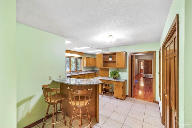 kitchen with light tile patterned flooring, a textured ceiling, kitchen peninsula, and a breakfast bar