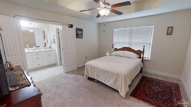 bedroom with light carpet, baseboards, connected bathroom, ceiling fan, and a tray ceiling