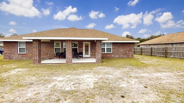 back of property with brick siding, roof with shingles, a patio area, and fence