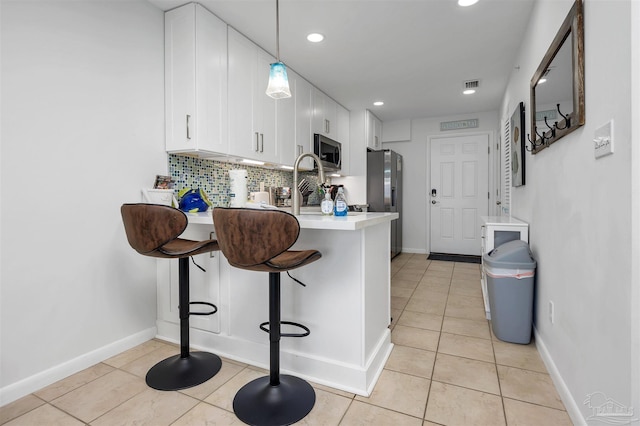 kitchen with pendant lighting, stainless steel appliances, light countertops, light tile patterned flooring, and white cabinets