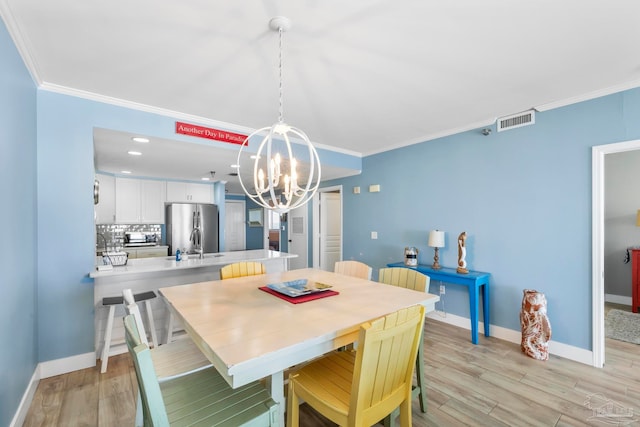 dining area with sink, an inviting chandelier, ornamental molding, and light wood-type flooring