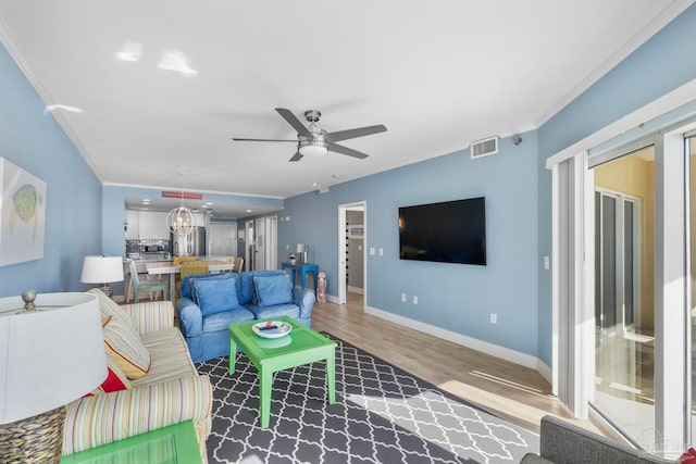 living room with wood-type flooring, ceiling fan with notable chandelier, and ornamental molding