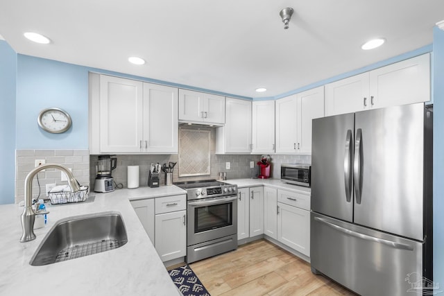 kitchen with white cabinetry, sink, backsplash, light hardwood / wood-style floors, and appliances with stainless steel finishes