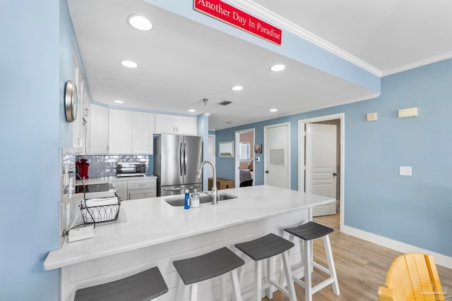 kitchen featuring sink, white cabinetry, stainless steel fridge, light hardwood / wood-style floors, and kitchen peninsula