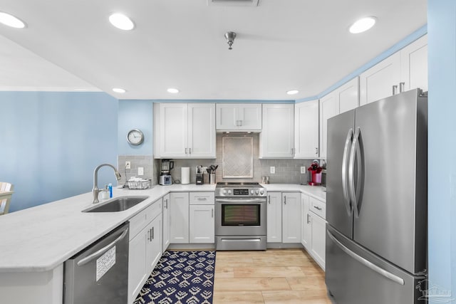 kitchen featuring kitchen peninsula, appliances with stainless steel finishes, sink, white cabinets, and light hardwood / wood-style floors