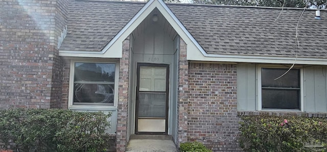 view of exterior entry with a shingled roof and brick siding