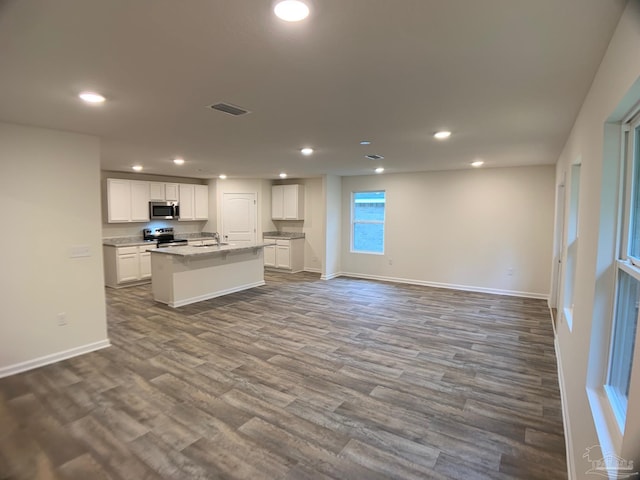 kitchen with appliances with stainless steel finishes, recessed lighting, a kitchen island with sink, baseboards, and white cabinets