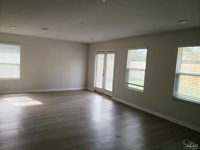 spare room with baseboards, healthy amount of natural light, and dark wood-type flooring