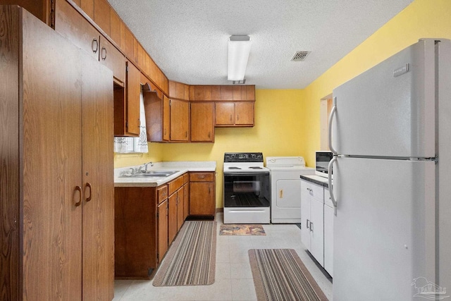 kitchen featuring white appliances, sink, light tile patterned floors, a textured ceiling, and washer / dryer