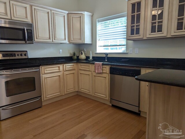 kitchen with dark stone countertops, light hardwood / wood-style flooring, cream cabinets, stainless steel appliances, and sink