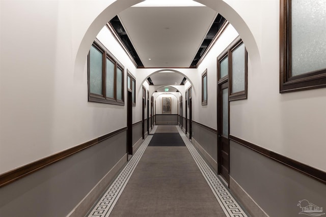 corridor with arched walkways and a wainscoted wall
