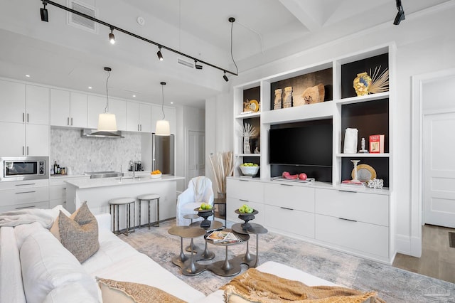 living room featuring beam ceiling, built in shelves, light hardwood / wood-style floors, track lighting, and sink