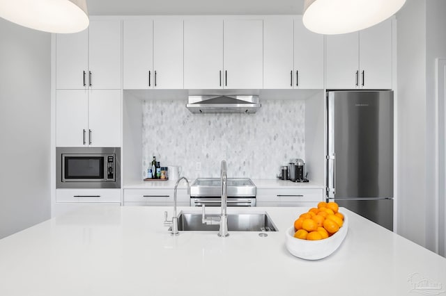 kitchen featuring wall chimney range hood, backsplash, white cabinetry, stainless steel appliances, and light countertops