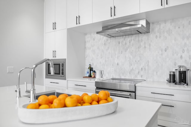 kitchen featuring white cabinetry, stainless steel microwave, wall chimney range hood, and stove