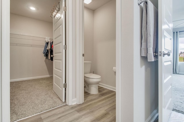 bathroom featuring a walk in closet, baseboards, toilet, and wood finished floors