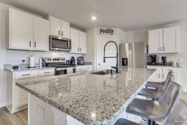 kitchen featuring appliances with stainless steel finishes, white cabinets, a sink, and light stone countertops