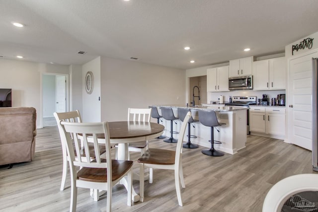 dining area featuring light wood-style floors, recessed lighting, visible vents, and a textured ceiling