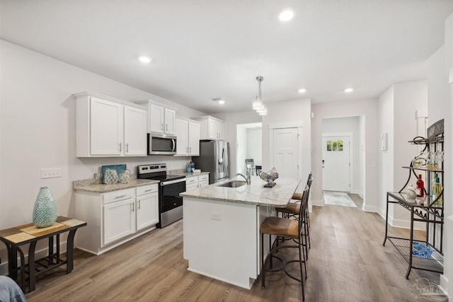 kitchen with white cabinets, sink, a center island with sink, light hardwood / wood-style floors, and appliances with stainless steel finishes