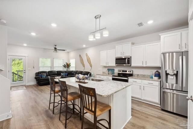 kitchen featuring appliances with stainless steel finishes, light wood-type flooring, white cabinets, and light stone countertops