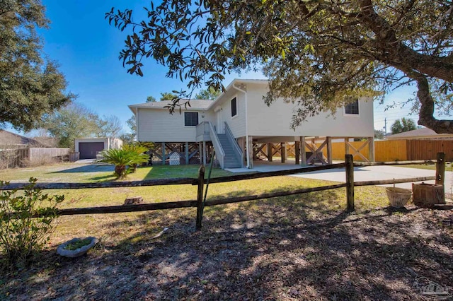 back of house featuring stairs, driveway, a lawn, and fence