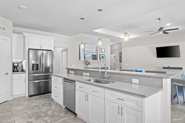 kitchen featuring a sink, white cabinets, open floor plan, appliances with stainless steel finishes, and decorative light fixtures