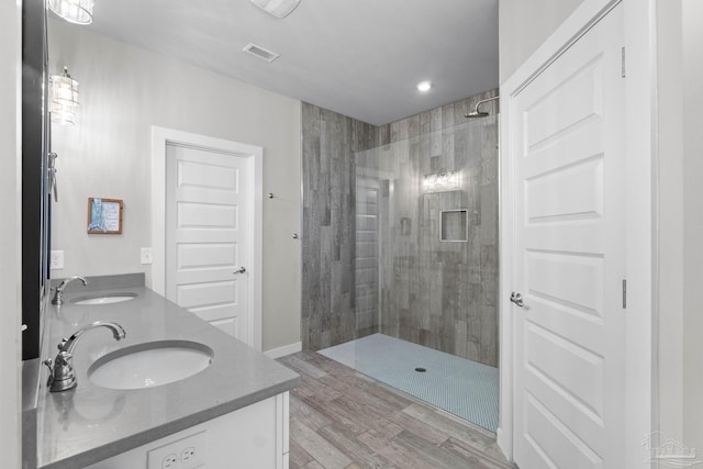 full bath with visible vents, a sink, a tile shower, and double vanity