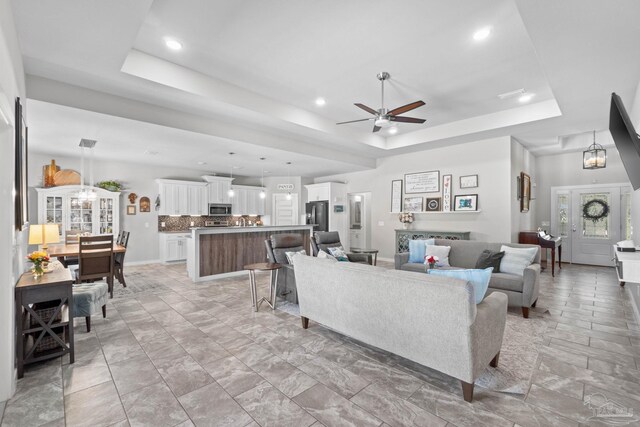 living room featuring baseboards, a tray ceiling, a ceiling fan, and recessed lighting