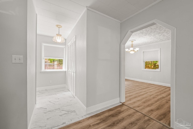 hall with ornamental molding, baseboards, marble finish floor, and a notable chandelier