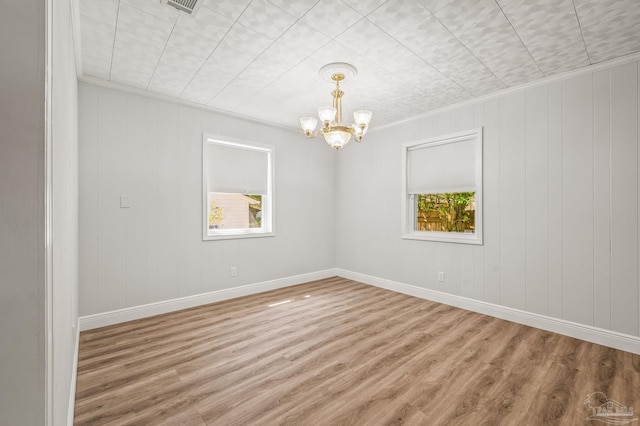 empty room featuring wood finished floors, an inviting chandelier, and ornamental molding