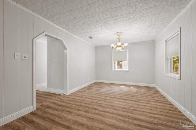 empty room with ornamental molding, arched walkways, a notable chandelier, and wood finished floors