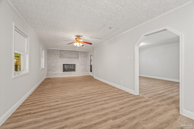 unfurnished living room featuring crown molding, light wood-style floors, arched walkways, a ceiling fan, and a brick fireplace