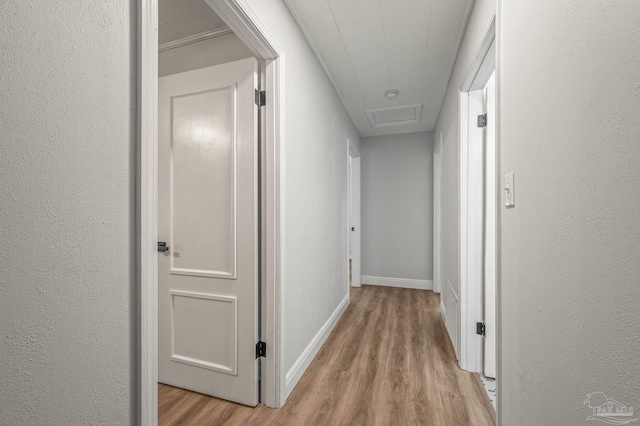 corridor with light wood-style flooring, attic access, and baseboards