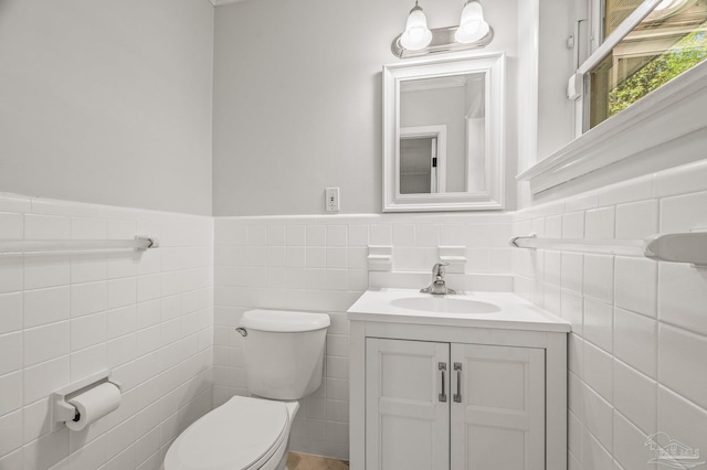 half bath with vanity, tile walls, a wainscoted wall, and toilet
