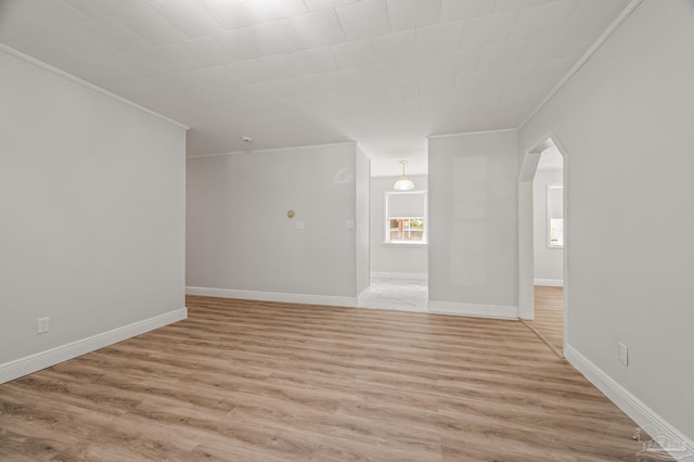 unfurnished room with arched walkways, light wood finished floors, baseboards, and crown molding