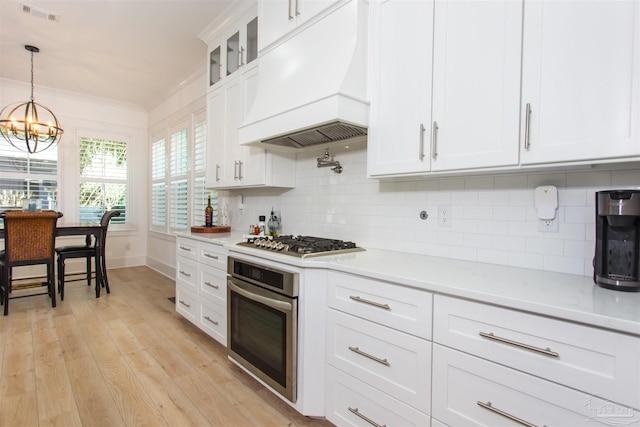 kitchen featuring visible vents, premium range hood, ornamental molding, stainless steel appliances, and a chandelier