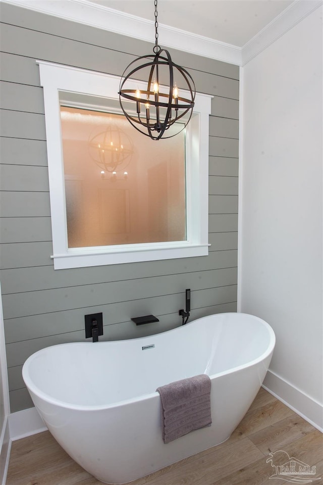 bathroom with wood finished floors, baseboards, an inviting chandelier, a freestanding bath, and crown molding