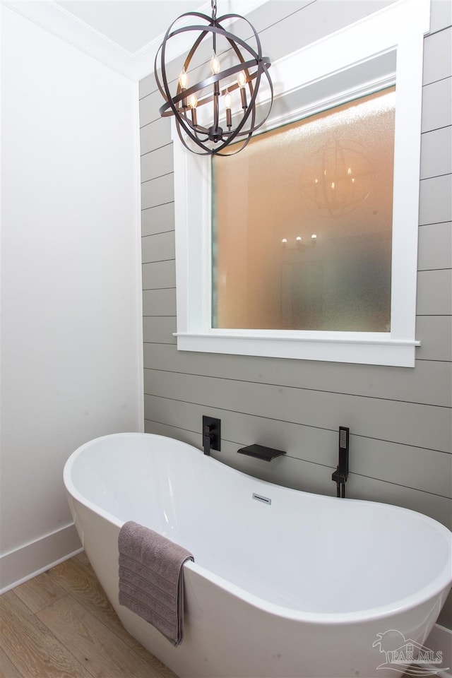 bathroom with wood finished floors, wooden walls, crown molding, a freestanding bath, and a chandelier