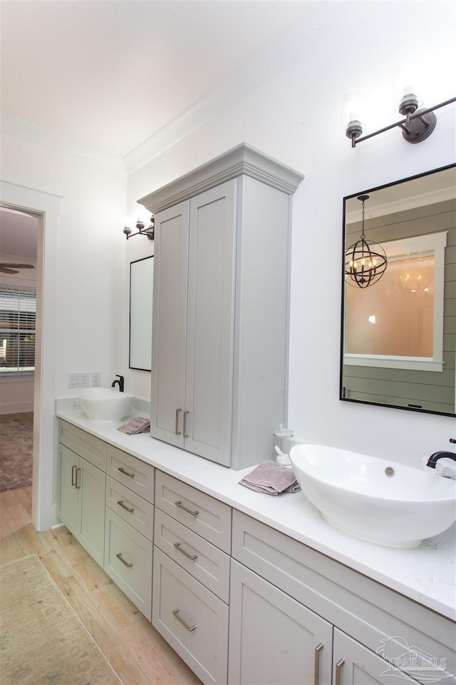 full bath with a sink, wood finished floors, double vanity, and ornamental molding