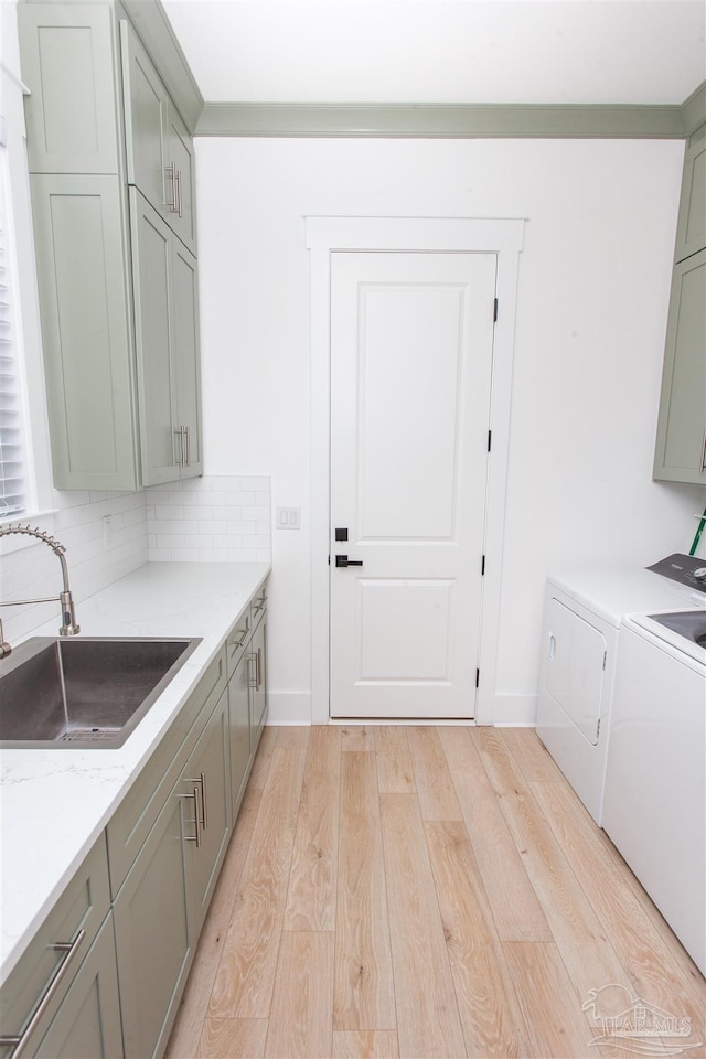 laundry area with washing machine and clothes dryer, baseboards, light wood-style floors, cabinet space, and a sink