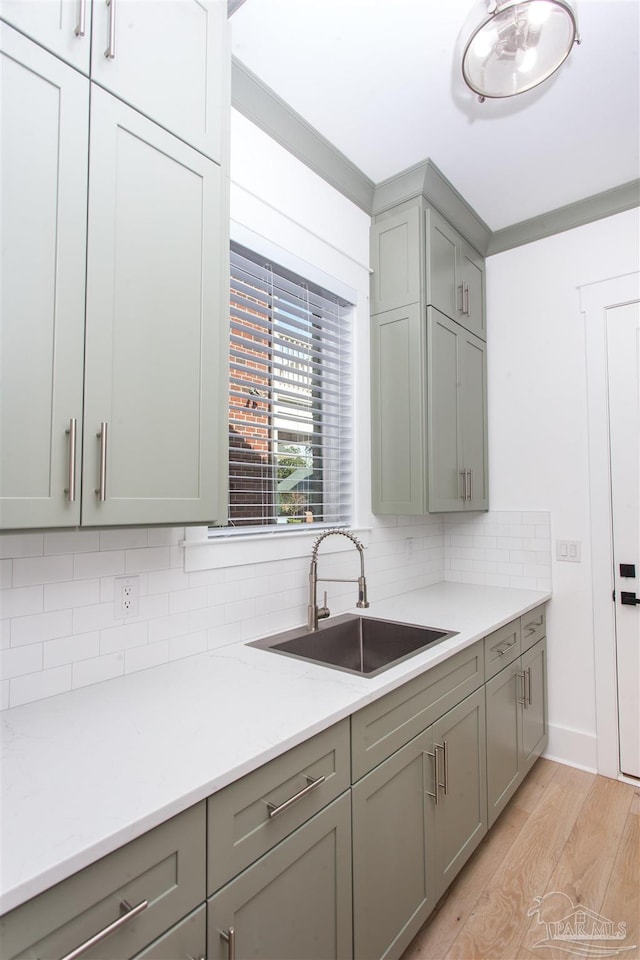 kitchen featuring light wood-type flooring, gray cabinetry, a sink, light countertops, and decorative backsplash