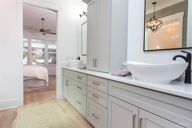 ensuite bathroom with ceiling fan with notable chandelier, wood finished floors, ensuite bathroom, and a sink