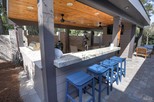 view of patio featuring a ceiling fan, exterior kitchen, fence, and outdoor wet bar