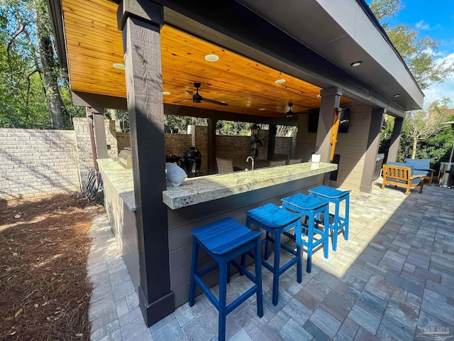 view of patio with a bar, a ceiling fan, and fence