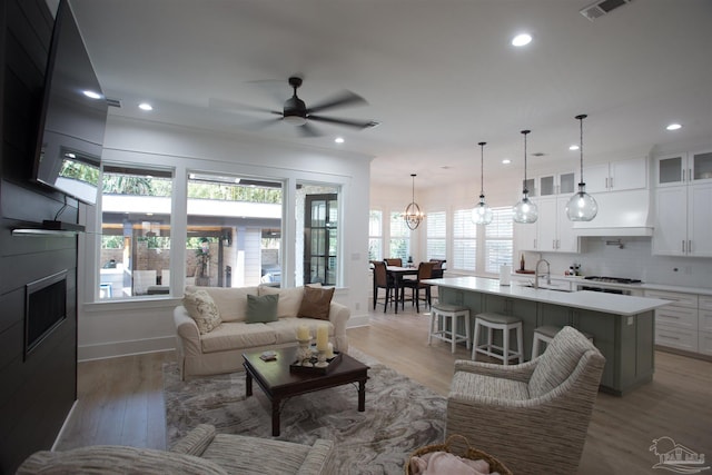 living area with visible vents, ceiling fan with notable chandelier, recessed lighting, a large fireplace, and light wood-style floors