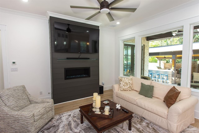 living room featuring wood finished floors, a ceiling fan, visible vents, ornamental molding, and a large fireplace