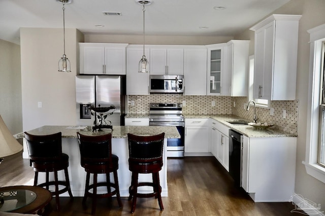 kitchen featuring white cabinets, a kitchen island, decorative light fixtures, and appliances with stainless steel finishes