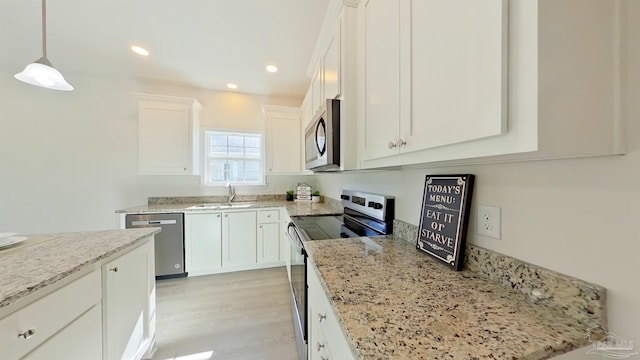 kitchen with stainless steel appliances, sink, decorative light fixtures, light hardwood / wood-style floors, and white cabinetry