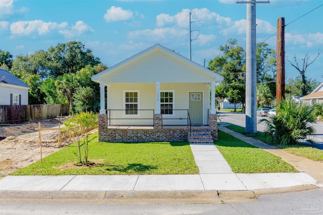 view of front of home with covered porch, a front lawn, and fence